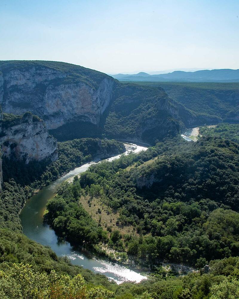 [Translate to Anglais:] Panoramic high angle view of the green Ardeche river canyon winding through deep forests and massive stone cliffs near Les Castels campsites.