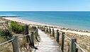 [Translate to Anglais:]  A scenic wooden boardwalk with rope railings cutting through sand dunes, near a luxury Les Castels campsite