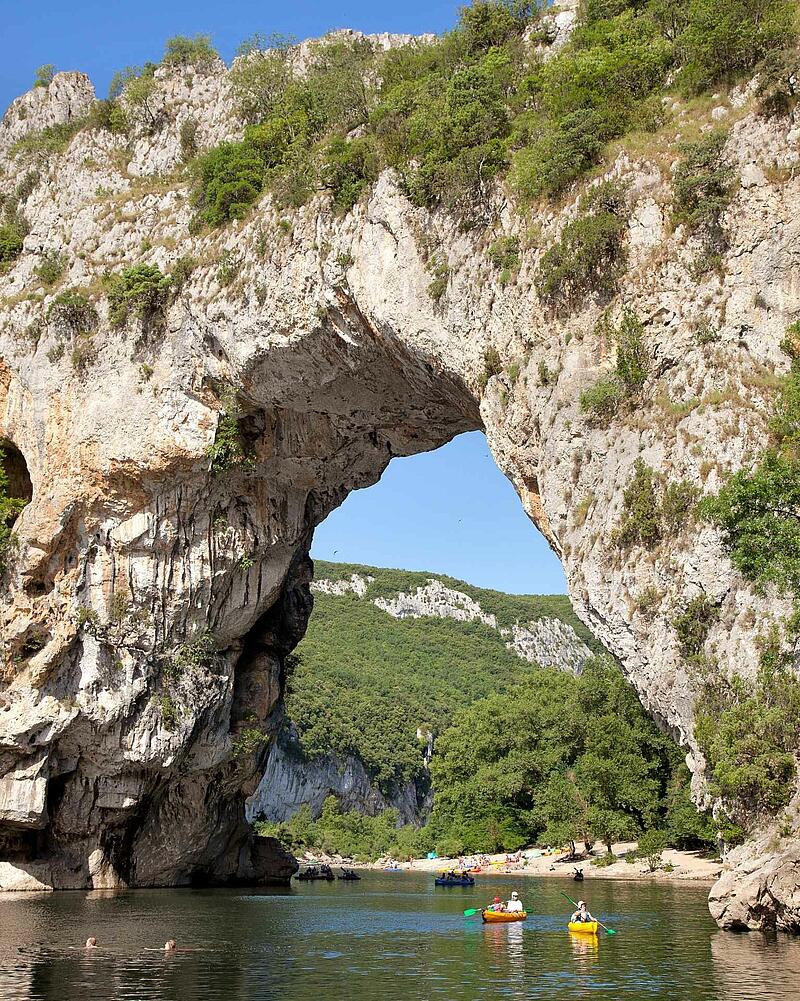 [Translate to Anglais:] Kayaks and canoes floating on the river under the massive, natural limestone arch of the Pont d'Arc in the spectacular Ardèche Gorges.