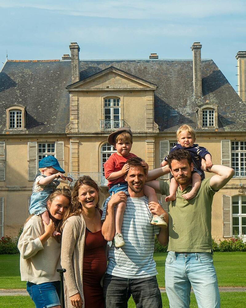 [Translate to Anglais:] A joyful group photo of adults and young children smiling together in front of a historic French chateau at a luxury Les Castels holiday estate.